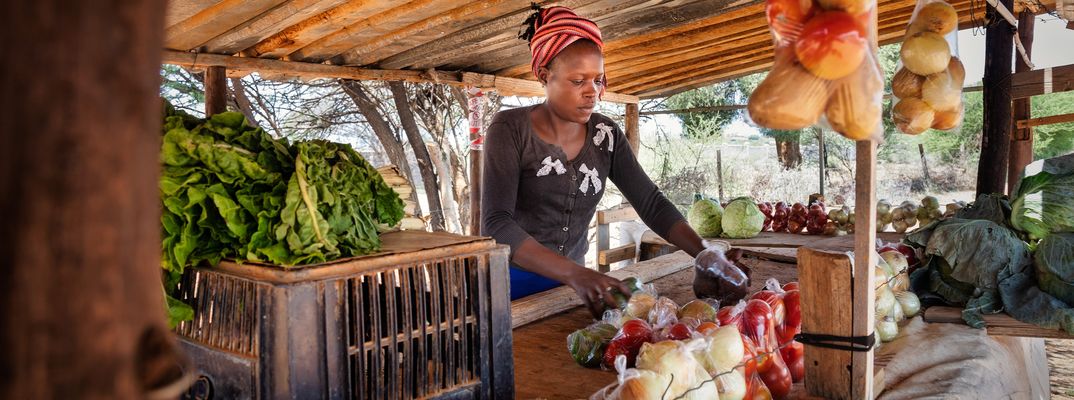 Eine Frau steht hinter einer Theke und verpackt Gemüse.