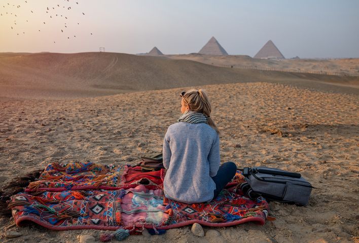 Frau sitzt auf einer Decke in der Wüste von Ägypten und blickt auf Pyramiden