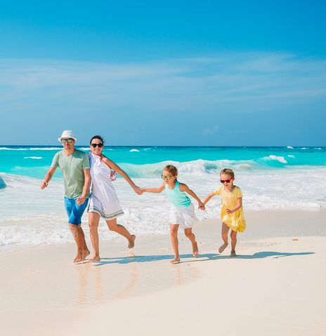 Eine Familie mit zwei Kindern läuft fröhlich durch die Wellen am Strand