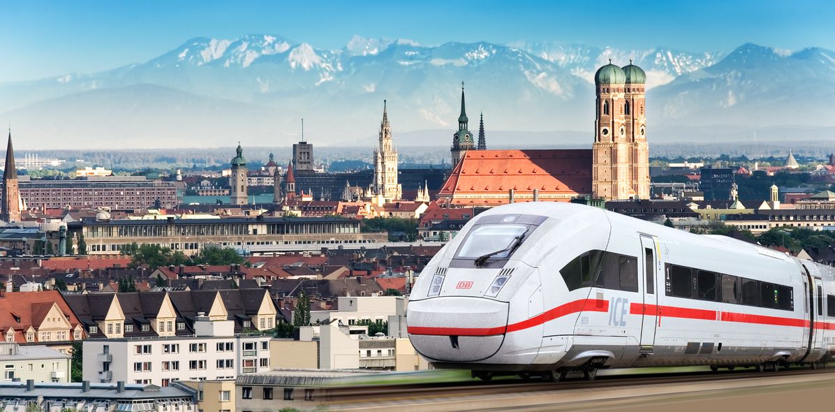 Panoramabild von München mit Frauenkirche und Bergen mit einen ICE im Vordergrund