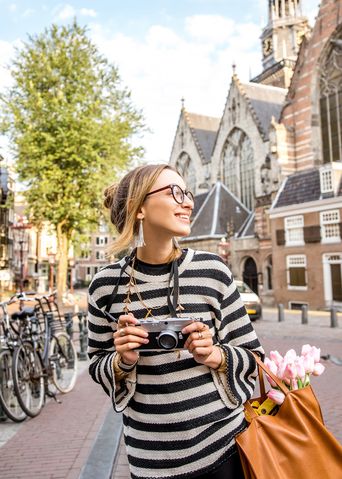 Frau beim Sightseeing in Amsterdam mit einer Kamera in der Hand und Tulpen in der Handtasche