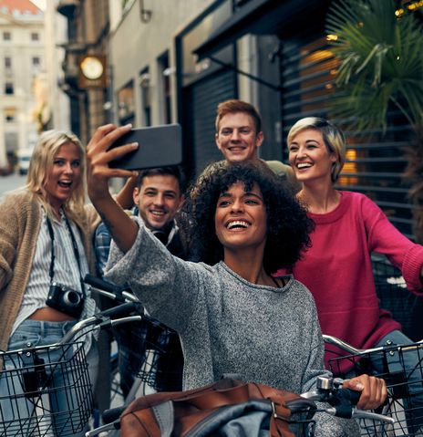 Gruppe junger Menschen fährt lachend mit Fahrrädern durch eine sonnige Altstadt