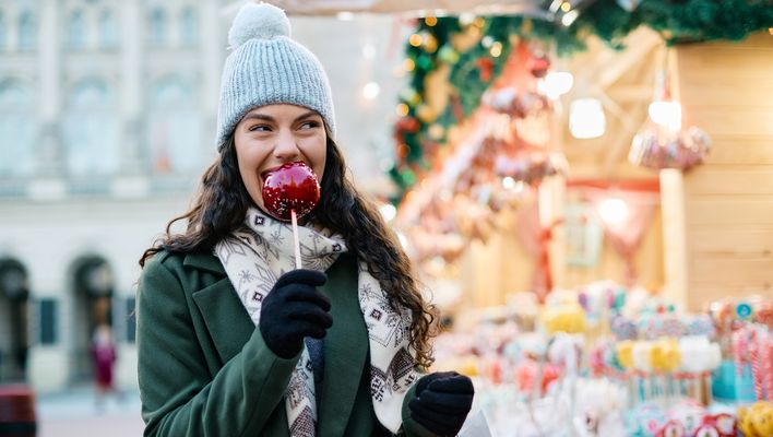 Eine Frau genießt einen glasierten Apfel auf dem Weihnachtsmarkt