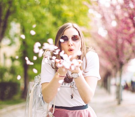 Eine Frau pustet rosafarbene Kirschblüten von ihren Händen in Richtung Kamera
