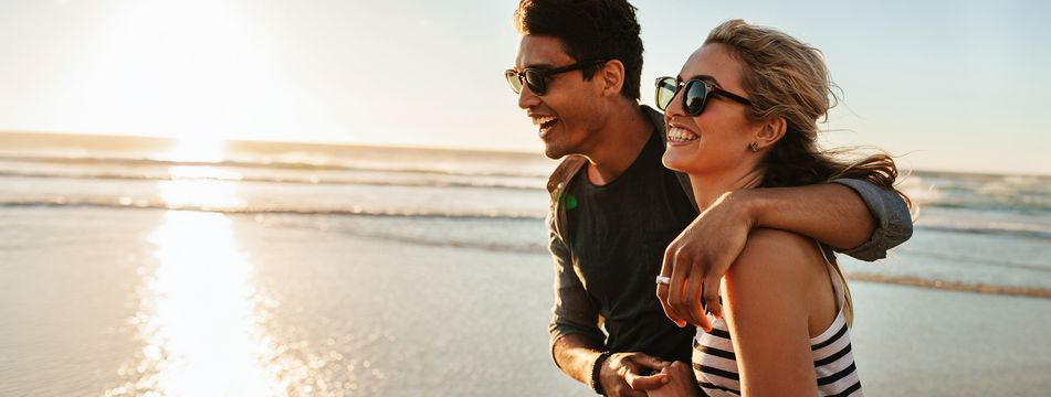 Glückliches Paar mit Sonnenbrillen bei einem Spaziergang am Strand