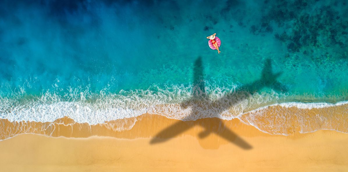 Flugzeugschatten am Strand über Frau im Meer