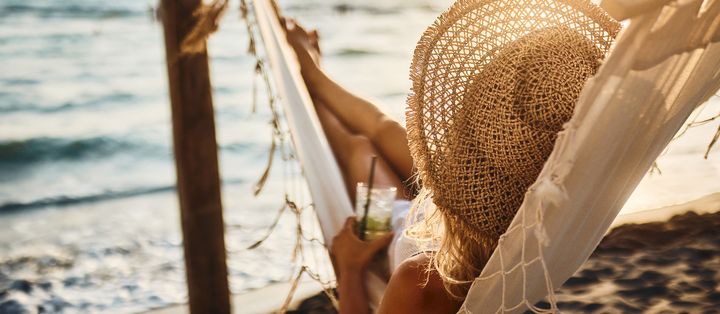 Frau liegt in einer Hängematte am Strand mit einem Cocktail in der Hand