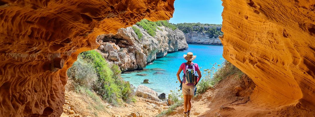 Wanderer auf Mallorca mit Rucksack auf dem Weg zu einer türkisblauen Bucht durch eine Felsöffnung