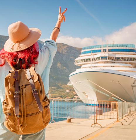 Frau steht mit Rucksack an Anlegestelle eines Kreuzfahrtschiffes
