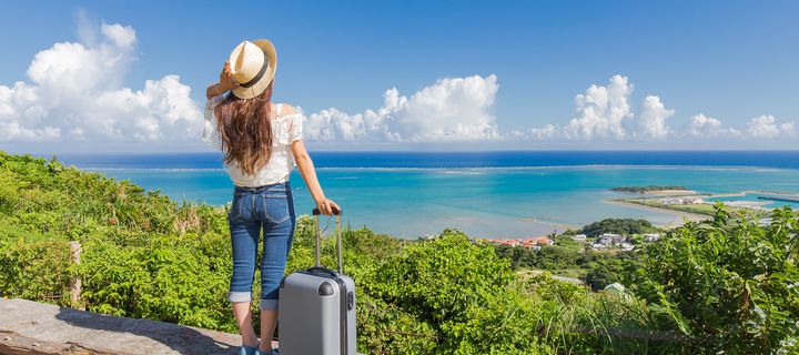 Frau mit Koffer am Strand mit Blick auf das Meer