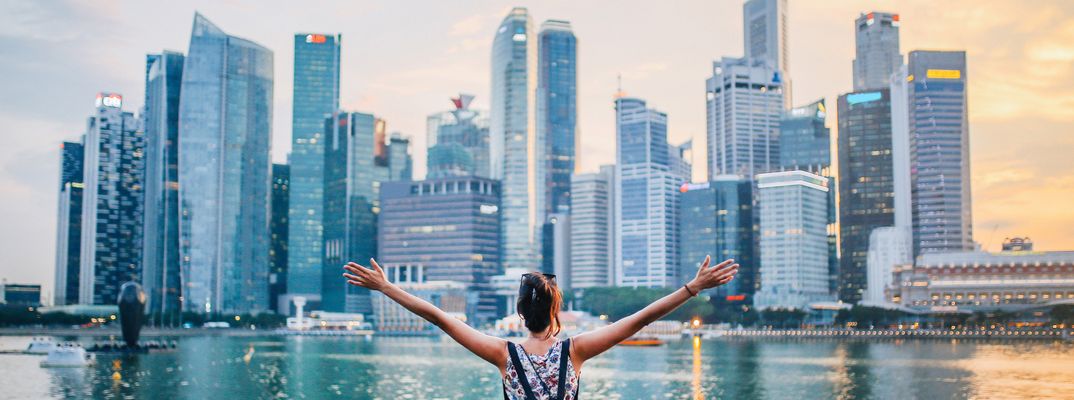 Frau steht mit ausgestreckten Armen vor der Skyline von Singapur mit modernen Wolkenkratzern am Wasser