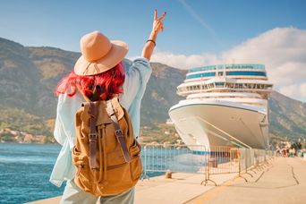 Eine Frau mit pinken Haaren winkt einem Kreuzfahrtschiff am Anleger zu
