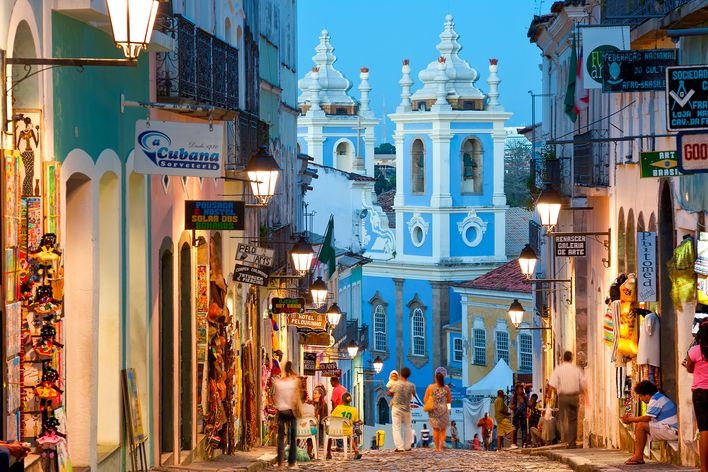 Kopfsteinpflastergasse mit bunten Häusern und einer blauen Kirche im historischen Pelourinho-Viertel von Salvador da Bahia, Brasilien