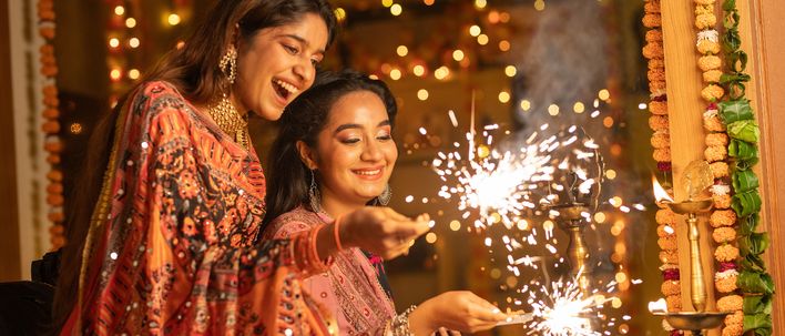 Zwei Frauen feiern Diwali mit Wunderkerzen in festlich geschmücktem Raum