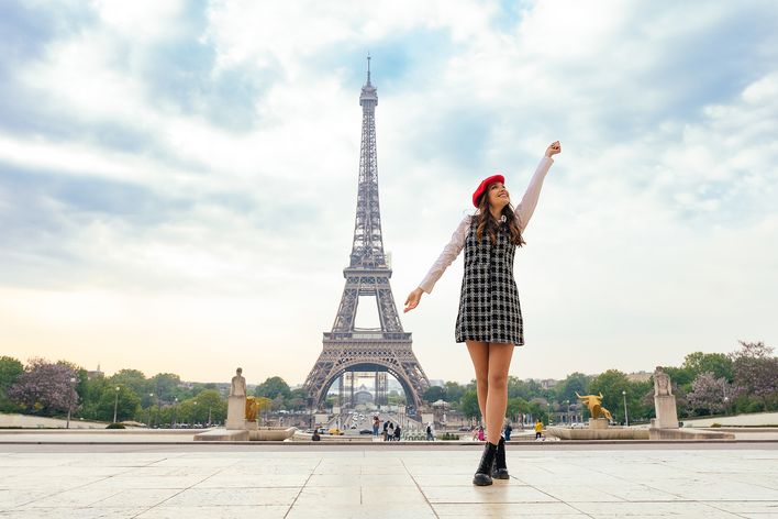 Frau steht mit ausgestreckten Armen vor dem Eiffelturm in Paris 