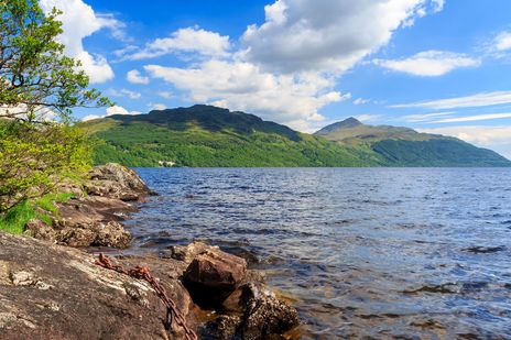 Ufer von Loch Lomond mit Steinen, Wasser und bewaldeten Hügeln