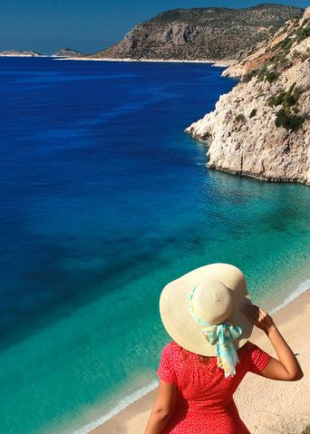 Frau mit Sonnenhut blickt auf eine Bucht an der türkischen Küste