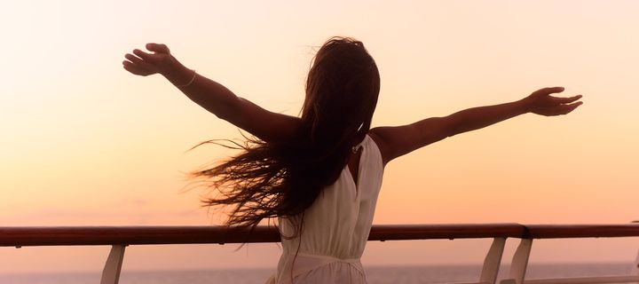 Frau mit ausgestreckten Armen an Decke eines Kreuzfahrtschiffs bei Sonnenuntergang