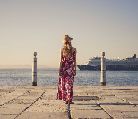Eine Frau steht zwischen den Säulen am Cais das Colunas und betrachtet ein Schiff auf dem Tejo