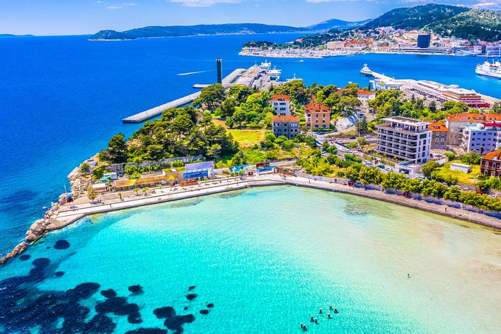 Luftaufnahme des Bačvice-Strandes in Split, Kroatien, mit türkisfarbenem Wasser, Häusern und Hafen im Hintergrund