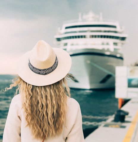 Frau steht mit dem Rücken zur Kamera vor einem Kreuzfahrtschiff, welches am Pier liegt
