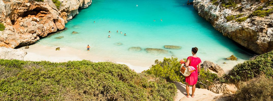 Frau blickt auf die Badebucht Calo des Moro mit türkisfarbenem Wasser und Felsen