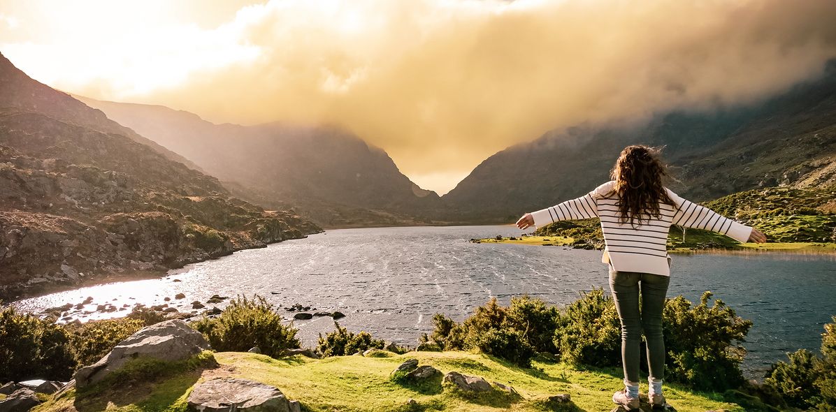 Frau auf Felsen schaut auf See in Irland