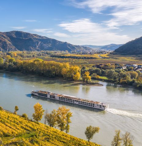 Flusskreuzfahrtschiff fährt entlang der Donau in Österreich mit Weinbergen am Ufer