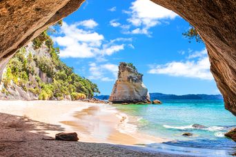 Die Cathedral Cove auf der Coromandel-Halbinsel rahmt einen hellen Strand und einen Felsen im Meer ein.