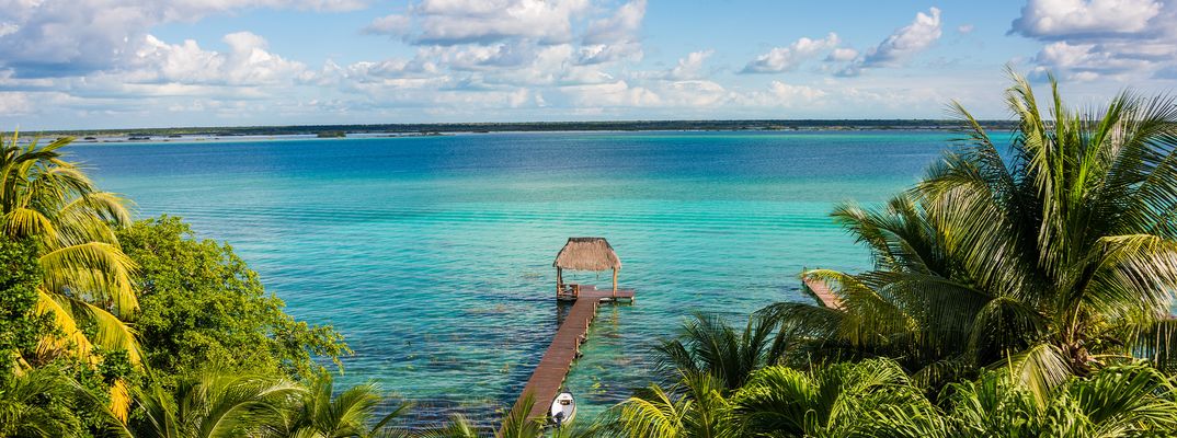 Blick auf die Lagune von Bacalar mit Holzsteg und Palmen 