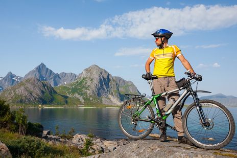 Radfahrer fährt auf einer Bergstraße mit Blick auf schroffe Gipfel und Wasser