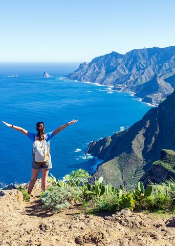 Frau mit ausgebreiteten Armen auf einer Klippe vor der Küste von Teneriffa auf den Kanaren