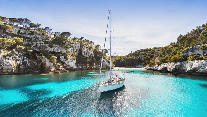 Boot in der Bucht Cala Macarella auf Menorca mit klarem, türkisblauem Wasser, umgeben von Felsen und Pinien