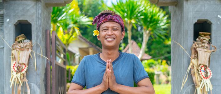 Balinesischer Mann begrüßt Gäste mit traditioneller Geste vor einem Tempeltor in Denpasar, Bali