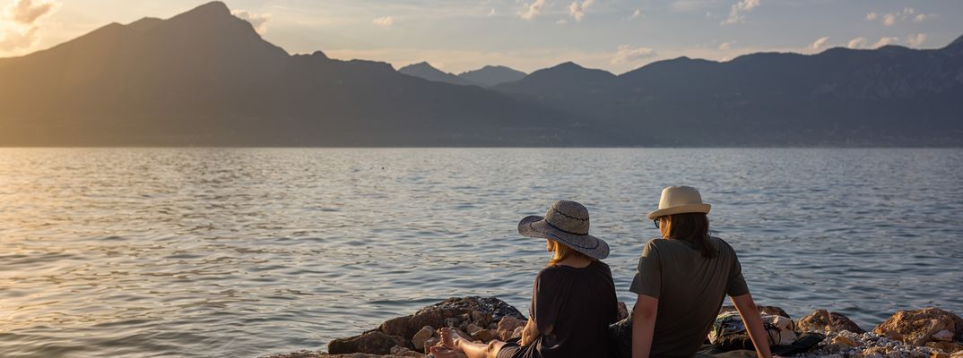 Paar sitzt am Ufer des Gardasees und genießt den Sonnenuntergang mit Blick auf die Berge