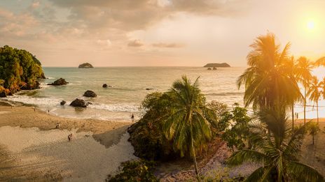 Tropischer Strand in Costa Rica bei Sonnenuntergang mit Palmen und Felsen am Wasser