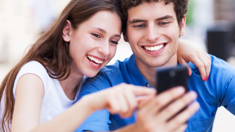 Frau und Mann gucken Arm in Arm interessiert in ein Handy und lachen