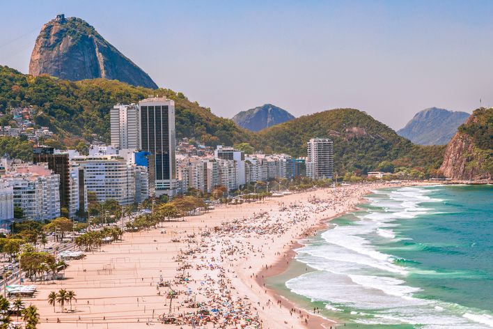 Copacabana-Strand in Rio de Janeiro mit zahlreichen Badegästen, türkisfarbenem Meer und dem Zuckerhut im Hintergrund