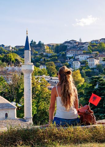Frau sitzt vor den Toren der historischen Altstadt von Gjirokastra, eine weitere UNESCO-Weltkulturerbestätte mit charakteristischen Häusern und Festung
