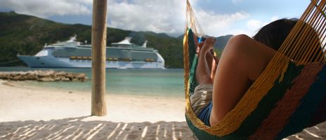 Frau liegt in einer Hängematte am Meer mit Blick auf ein Kreuzfahrtschiff im Sommer