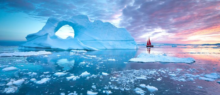 Leuchtend blauer Eisberg in Grönland mit Gletscherbogen und kaltem Polarmeer