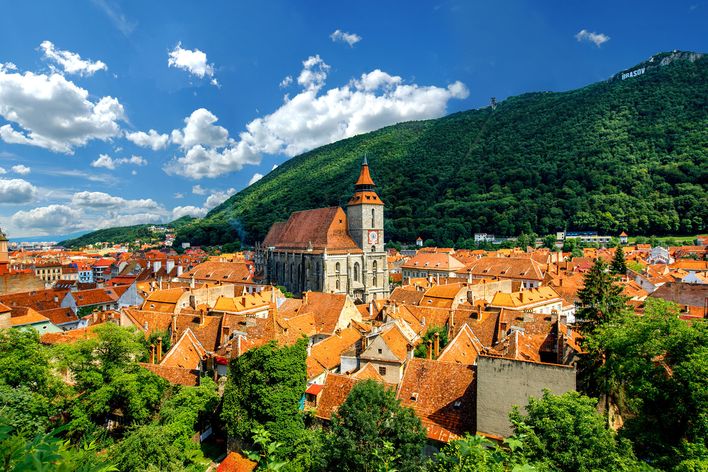 Rote Dächer und Kirchtürme prägen die Altstadt von Brașov vor grünen Bergen.