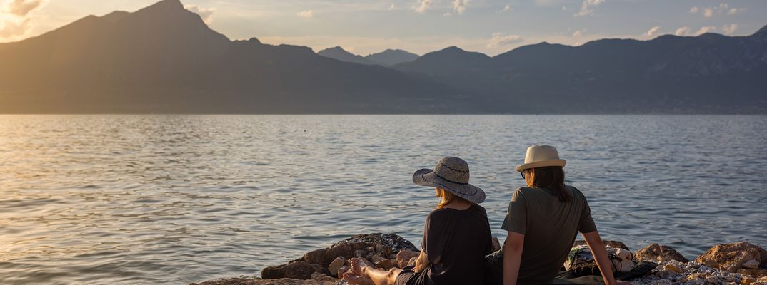 Paar sitzt am Ufer des Gardasees und genießt den Sonnenuntergang mit Blick auf die Berge