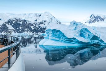Blick vom Expeditionskreuzfahrtschiff auf einen türkisblauen Eisberg und schneebedeckte Berge im Neko Harbour in der Antarktis