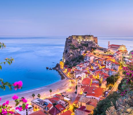 Panoramablick auf die Küste von Scilla in Kalabrien mit bunten Häusern am Hang, blauem Meer und pink blühenden Bougainvillea im Vordergrund