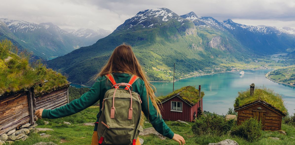 Eine Frau schaut auf den Fjord Rakssetra hinunter mit einer verschneiten Berglandschaft im Hintergrund