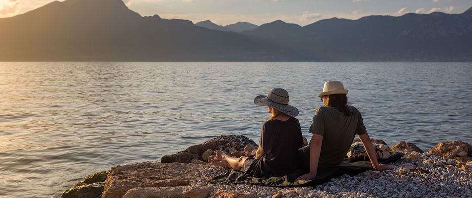 Paar sitzt am Ufer des Gardasees und genießt den Sonnenuntergang mit Blick auf die Berge