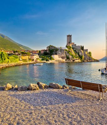 Strand in Malcesine am Gardasee mit Blick auf die Scaligerburg und Segelboot bei Sonnenuntergang