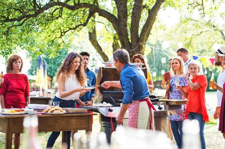 Gruppe von sommerlich gekleideten Menschen grillt in einem Park
