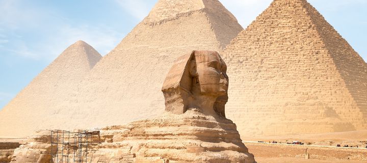 Die Sphinx und die Pyramiden von Gizeh vor blauem Himmel.